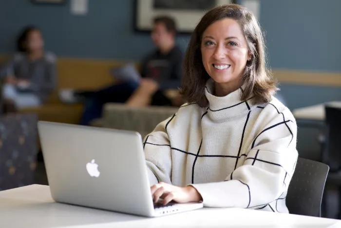 A woman sitting at a laptop and smiling at a camera