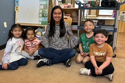 A female teacher sitting with four young children