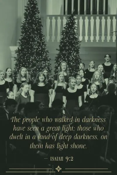 A choir of young women in black dresses sing in front of two decorated Christmas trees. Below is the text  - Isaiah 9:2