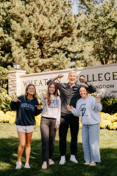 Student Ambassadors cheering in front of the Wheaton College sign.