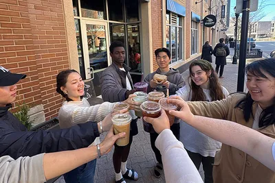 A group of seven people standing outside a café clink their drinks together