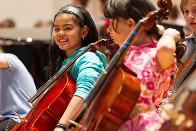 A couple of girls holding cellos and smiling
