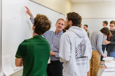 A physics professor teaches his students at the whiteboard.