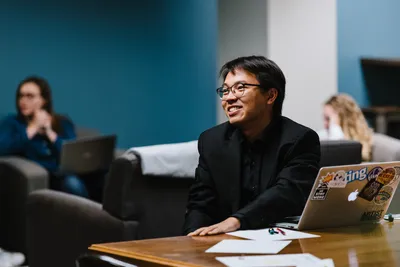 A man who is sitting at his laptop and looking to the side and smiling