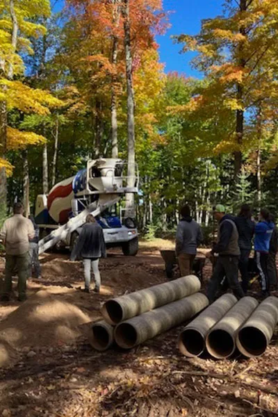 A group of people gathered around large pipes in front of some trees
