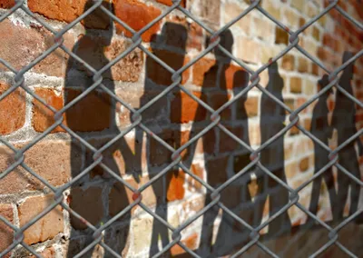 Shadows of incarcerated youth on brick wall behind fence