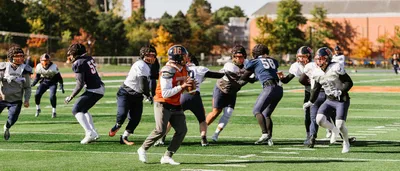 Football players practicing on a field on campus. A quarterback looks out over the field to make a pass.