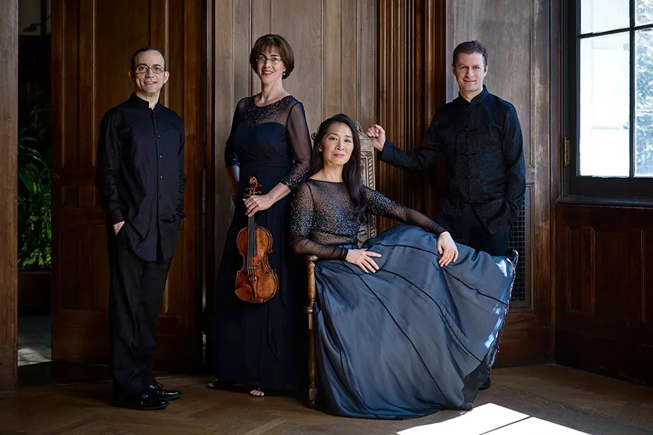 A group of four musicians stands together in a room, smiling