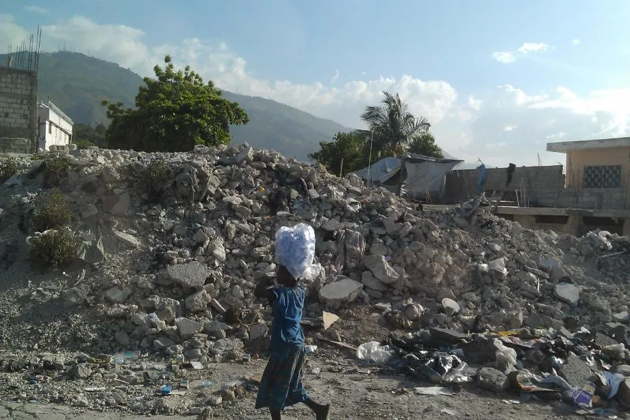 Boy balances bag on top of his head through rubble and fallen houses in Haiti after the earthquake