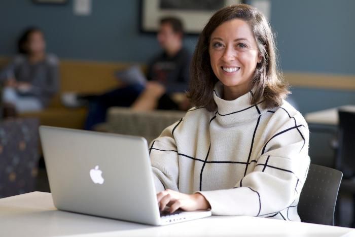 A woman sitting at a laptop and smiling at a camera