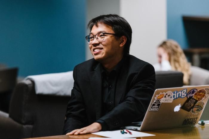 A man sitting at his laptop, looking to one side, and smiling