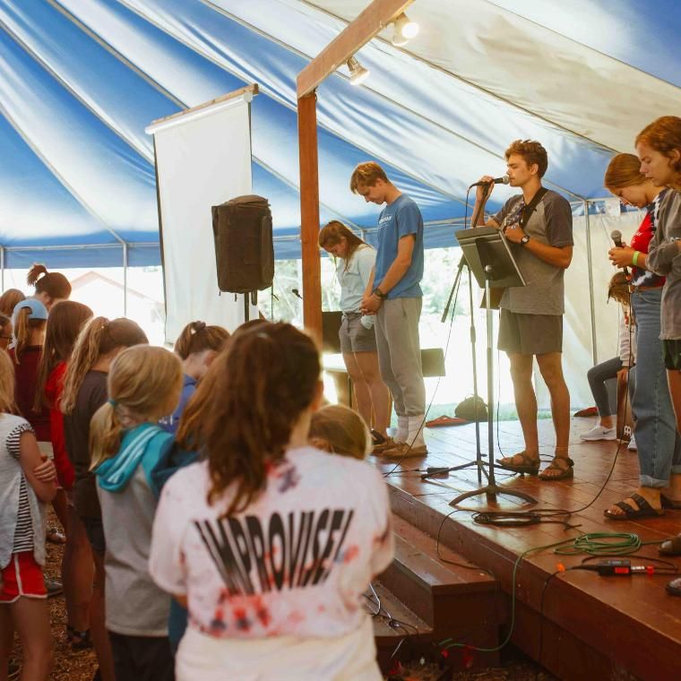 After group games, Day Campers sing fun worship songs in the blue and white tent.