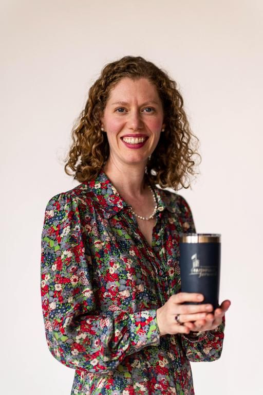Woman wearing multicolor floral dress holds branded Wheaton insulated mug