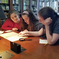 Three women reading by a desk